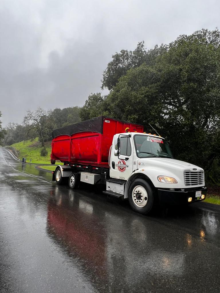 Independent Dumpster truck delivering a red dumpster in all weather conditions
